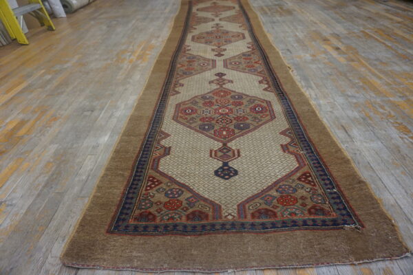 Geometric runner rug with a light beige field and brown border lying on distressed gray wood flooring.