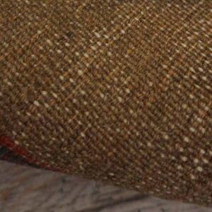 Close-up of a rug's brown woven backing with white flecks and visible red and blue pattern along the edge.