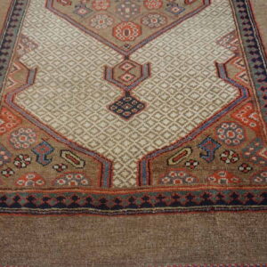 Brown rug with a cream diamond-patterned field bordered by geometric motifs in rust, navy, and light blue.