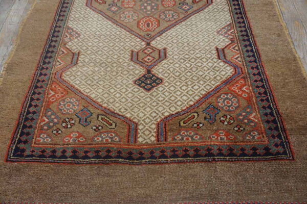 Brown rug with a cream diamond-patterned field bordered by geometric motifs in rust, navy, and light blue.