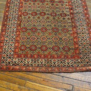 Tan rug with repeating red floral motifs and borders rests on rustic wood flooring.