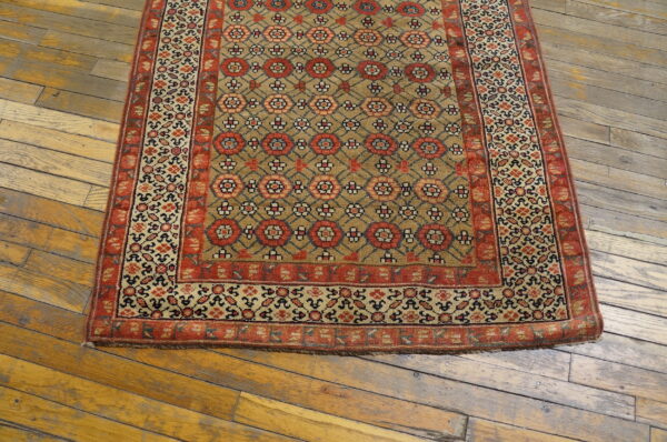 Tan rug with repeating red floral motifs and borders rests on rustic wood flooring.
