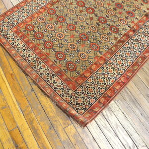 Low-pile rug in tan, red, and cream geometric patterns covers yellow-toned distressed wood floorboards.