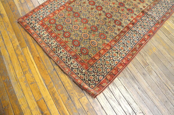 Low-pile rug in tan, red, and cream geometric patterns covers yellow-toned distressed wood floorboards.