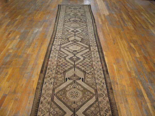 Geometric brown, tan, and cream runner rug displayed along distressed orange-toned hardwood flooring.