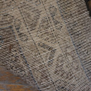 Close-up showing the ribbed, woven reverse side of a rug with brown and tan stripes on wood planks.