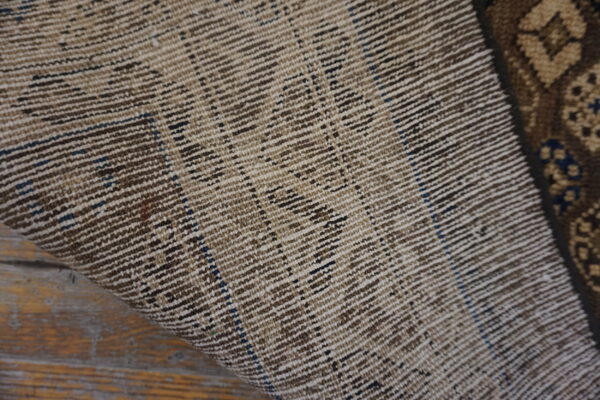 Close-up showing the ribbed, woven reverse side of a rug with brown and tan stripes on wood planks.