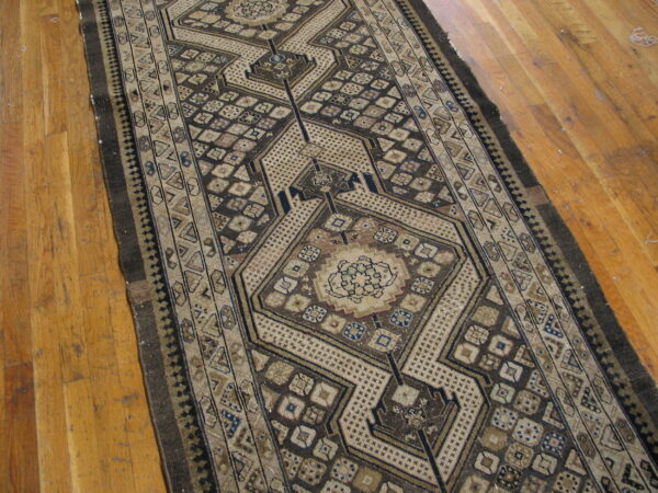 Long geometric runner rug in brown, beige, and blue with central medallions on light wood flooring.