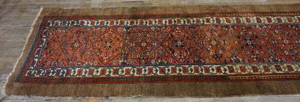 Red and blue patterned runner with wide brown edges resting on rustic gray wood planks.