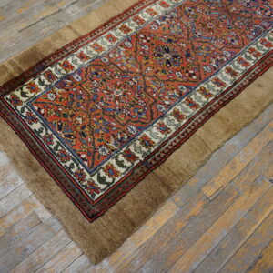 Traditional orange and blue patterned runner with a wide, shaggy brown border rests on distressed gray wood.