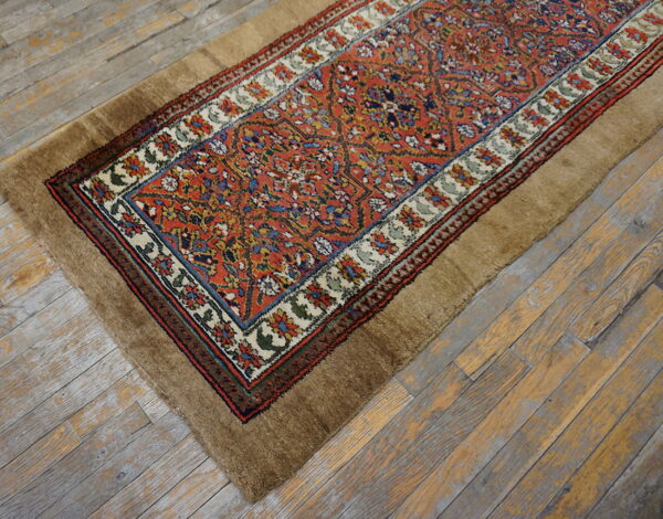 Traditional orange and blue patterned runner with a wide, shaggy brown border rests on distressed gray wood.