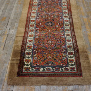A narrow runner rug with a red patterned center and a wide, high-pile brown border rests on distressed gray wood flooring.