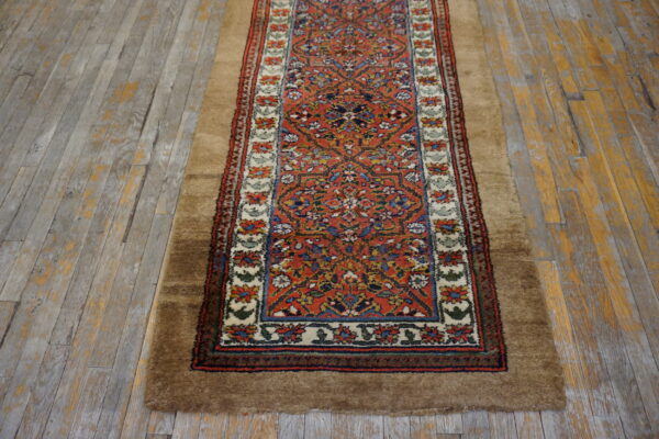 A narrow runner rug with a red patterned center and a wide, high-pile brown border rests on distressed gray wood flooring.