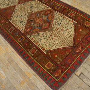 An intricate geometric rug in warm red and brown tones rests on light, distressed wooden flooring.