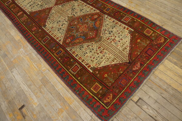 An intricate geometric rug in warm red and brown tones rests on light, distressed wooden flooring.