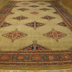 A long golden-tan rug featuring repeated navy and rust diamond motifs and elaborate floral borders on wood flooring.