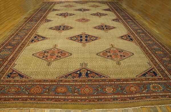 A long golden-tan rug featuring repeated navy and rust diamond motifs and elaborate floral borders on wood flooring.