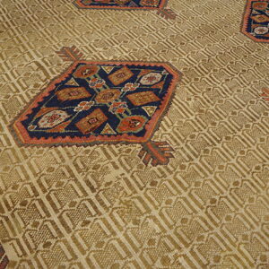 Tan rug with low pile geometric field texture and scattered octagonal motifs in navy, rust, and pink.