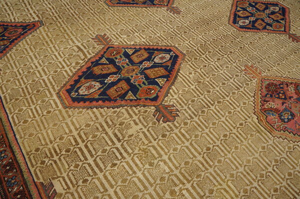 Tan rug with low pile geometric field texture and scattered octagonal motifs in navy, rust, and pink.