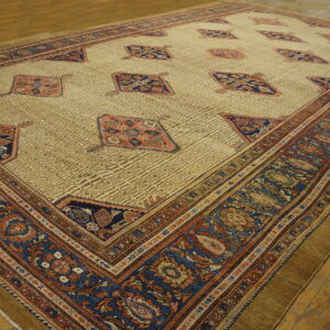 Low-pile rug with a pale gold field, featuring blue and rust medallions, displayed on wood floors.
