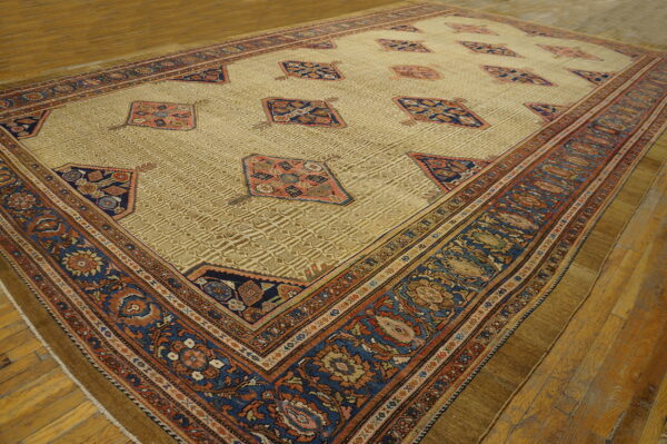 Low-pile rug with a pale gold field, featuring blue and rust medallions, displayed on wood floors.