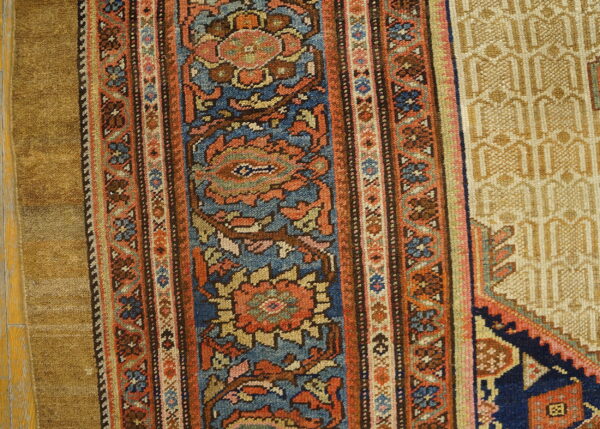 Intricate rug detail showing blue and rust floral borders, a tan geometric field, and distressed wood flooring.
