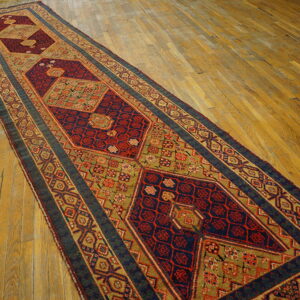 Geometric runner rug in deep red, navy, and moss green colors laid diagonally on wood planks.