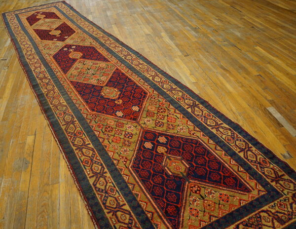 Geometric runner rug in deep red, navy, and moss green colors laid diagonally on wood planks.