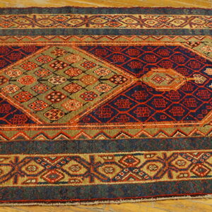 A traditional runner rug with navy, red, olive, and tan geometric diamonds lies on a wood floor.