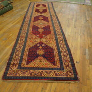 Traditional runner rug with red, navy, and khaki geometric motifs displayed on worn wood flooring.