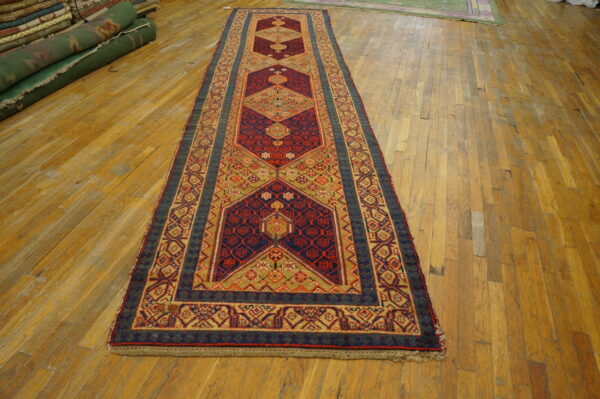 Traditional runner rug with red, navy, and khaki geometric motifs displayed on worn wood flooring.