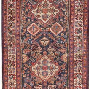 Narrow runner rug featuring a dense geometric design in navy, red, and beige, with an ornate floral border.