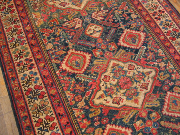 Dark blue rug featuring complex red, cream, and gold geometric and floral patterns on wood flooring.