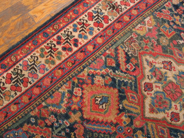 Corner detail of a low-pile rug with geometric patterns in deep blue, red, and cream on wood floors.