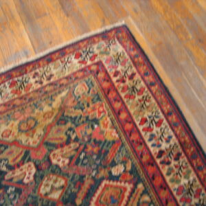 Intricate red, blue, and tan traditional rug corner laid over a diagonally running wooden floor.