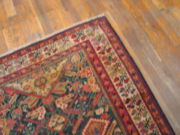 Intricate red, blue, and tan traditional rug corner laid over a diagonally running wooden floor.