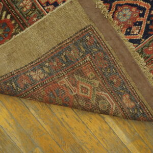 Traditional rug with red, navy, and green geometric patterns folded over aged hardwood flooring.