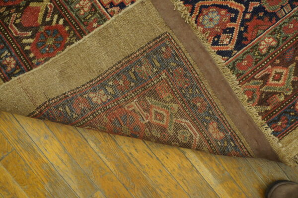 Traditional rug with red, navy, and green geometric patterns folded over aged hardwood flooring.
