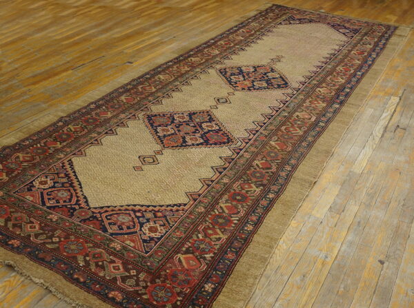Tan runner with navy and red geometric medallions and wide borders rests on distressed wood flooring.