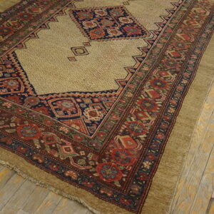 Geometric tan rug with red, navy, and brown complex borders lies on distressed light wooden floors.