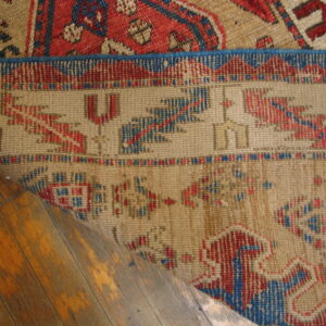 Low-pile geometric rugs in tan, red, and blue overlap on distressed wood plank flooring.