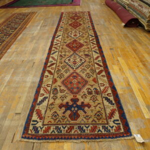 Tan, red, and blue geometric runner rug with a low pile on wide, distressed wooden floor planks.