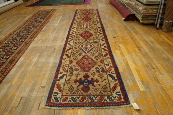 Tan, red, and blue geometric runner rug with a low pile on wide, distressed wooden floor planks.