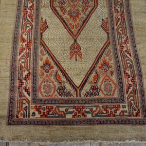 Khaki-colored rug with complex red and navy geometric patterns displayed on weathered wooden planks.