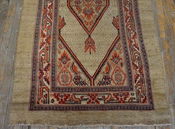 Khaki-colored rug with complex red and navy geometric patterns displayed on weathered wooden planks.