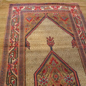 Low-pile tribal rug in beige, red, and navy with a central arch motif rests on light wood planks.