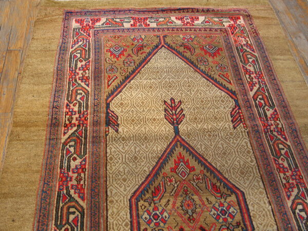 Low-pile tribal rug in beige, red, and navy with a central arch motif rests on light wood planks.