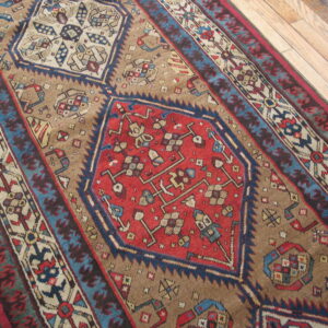 Close-up showing a colorful geometric rug in tan, red, and blue tones laid diagonally on wood planks.
