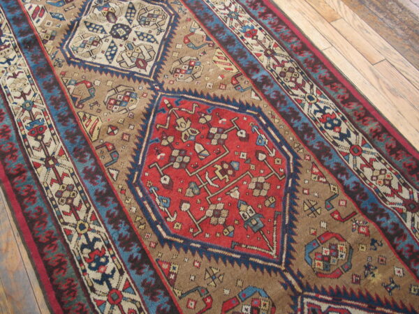Close-up showing a colorful geometric rug in tan, red, and blue tones laid diagonally on wood planks.
