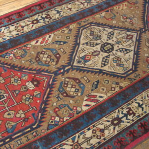 Geometric rug pattern featuring large red, blue, and tan stepped diamonds on a light wood floor.